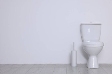 Beyaz duvarın yanında yerde tuvalet ve fırça var. Metin için boşluk