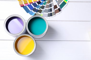 Parlak boya kutuları ve beyaz ahşap masa üzerinde renk paletleri, düz yatış. Metin için boşluk