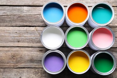 Cans of bright paints on wooden table, flat lay. Space for text