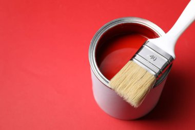 Can of bright paint and brush on red background, closeup. Space for text