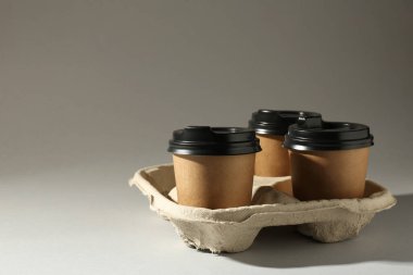 Paper coffee cups in cardboard holder on light grey background. Space for text