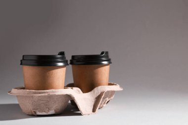 Paper coffee cups in cardboard holder on light grey background. Space for text