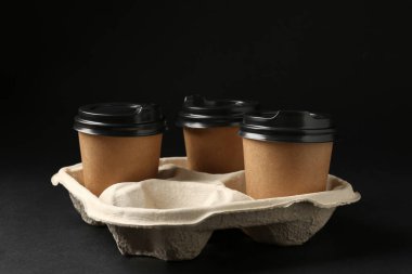 Kağıt kahve bardakları siyah arka planda karton tutucu, yakın plan.