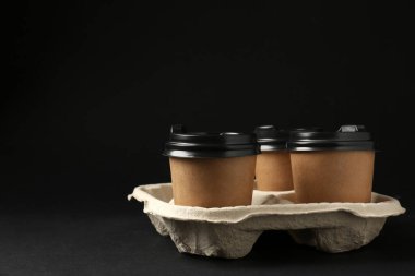 Siyah arka planda karton tutacakta kağıt kahve fincanları. Metin için boşluk