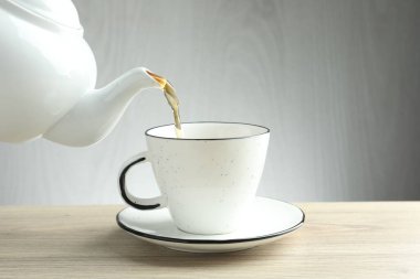 Tahta masada çaydanlıktan fincana taze demlenmiş çay dökülüyor, yakın plan.