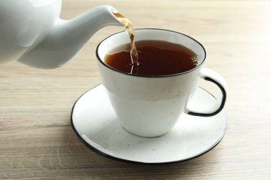 Tahta masada çaydanlıktan fincana taze demlenmiş çay dökülüyor, yakın plan.