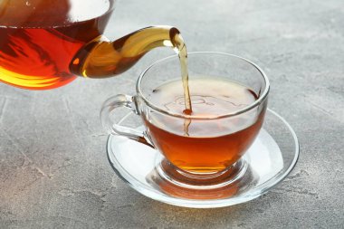Gri masada çaydanlıktan fincana taze demlenmiş çay dökülüyor, yakın plan.