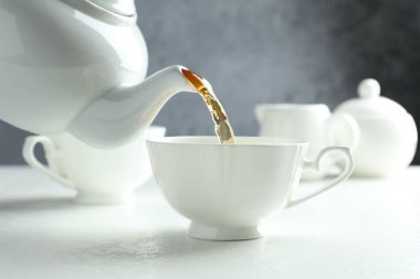 Beyaz masada çaydanlıktan fincana taze demlenmiş çay dökülüyor, yakın plan.