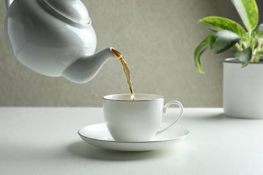 Beyaz masada çaydanlıktan fincana taze demlenmiş çay dökülüyor, yakın plan.