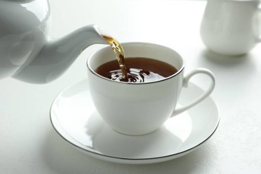 Beyaz masada çaydanlıktan fincana taze demlenmiş çay dökülüyor, yakın plan.