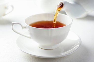 Beyaz masada çaydanlıktan fincana taze demlenmiş çay dökülüyor, yakın plan.