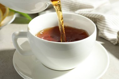 Hafif desenli masada çaydanlıktan fincana aromatik çay dökülüyor, yakın plan.