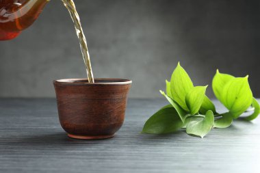 Siyah ahşap masada fincana aromatik çay dökülüyor. Gri arka plan, yakın plan.