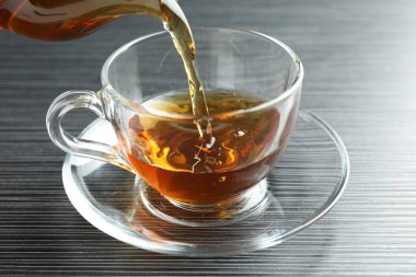 Siyah ahşap masada fincana aromatik çay dökülüyor, yakın plan.