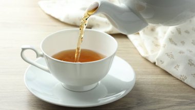 Ahşap masada çaydanlıktan fincana aromatik çay dökülüyor.