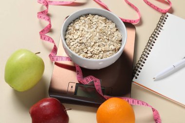 Elektronik mutfak ölçeği, mezura, not defteri ve bej masadaki ürünler, yakın plan. Kalori kontrolü