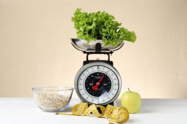 Ürünlerle birlikte mekanik mutfak terazisi ve bej arka planda beyaz ahşap masadaki şerit. Diyet