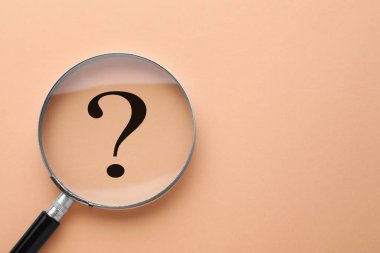 Şeftali rengi arka planda soru işareti, büyüteçle üstten görüntü. Metin için boşluk