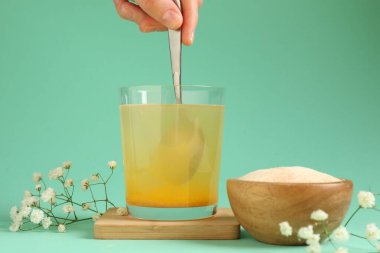 Turkuaz arka planda suda kolajen tozu karıştıran kadın, yakın plan.