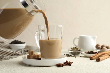 Beyaz desenli masada cam fincana aromatik Masala çayı dökülüyor, yakın plan.