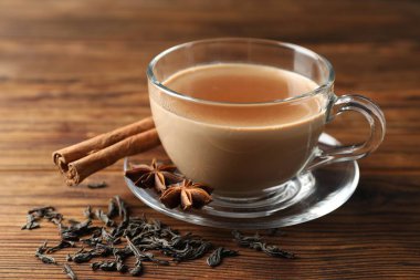 Bardakta Aromatik Masala çayı, ahşap masada baharatlar ve kuru yapraklar, yakın plan.