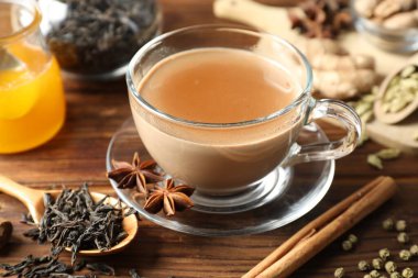 Aromatik Masala çayı fincanda, baharatlar, kuru yapraklar ve bal ahşap masada, yakın plan.