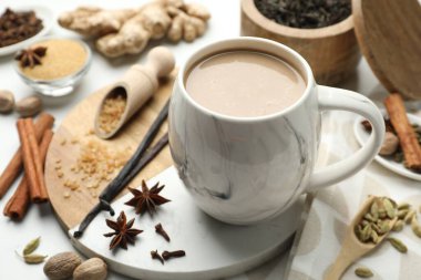 Beyaz masa üzerinde kahverengi şeker ve baharatlar, fincanda Aromatik Masala çayı.
