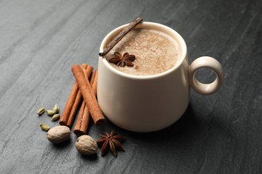Fincanda Aromatik Masala çayı ve siyah masada baharatlar, yakın plan.