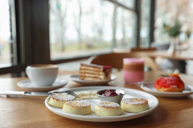 Lezzetli süzme peynir krepleri, tatlılar ve kafedeki ahşap masada servis edilen aromatik kahve.