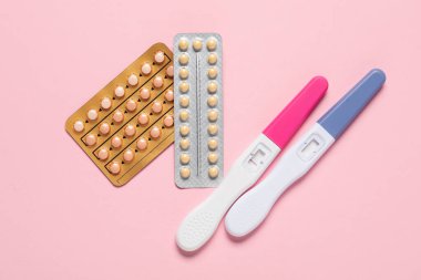 Blisters of oral contraceptive pills and pregnancy tests on pink background, flat lay