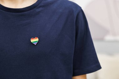 Kapalı alanda LGBT bayrağı renginde kalp şeklinde iğnesi olan adam, yakın plan