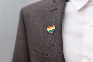 Kapalı alanda LGBT bayrağı renginde kalp şeklinde iğnesi olan adam, yakın plan