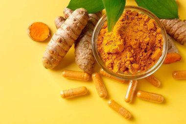 Sarı zemin üzerinde zerdeçal kapsülleri, toz, kökler ve yeşil yapraklar, düz zemin