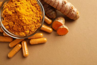 Zerdeçal kapsülleri, toz ve kökler bej arka planda, düz yerde. Metin için boşluk