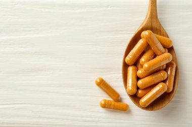 Beyaz ahşap masada kaşık içinde zerdeçal kapsülleri, üst manzara. Metin için boşluk