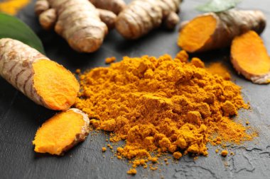 Aromatik zerdeçal tozu ve siyah masanın üzerinde taze kökler, yakın plan.