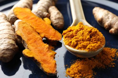 Kaşıkta aromatik zerdeçal tozu ve mavi tabakta taze kökler, yakın plan.