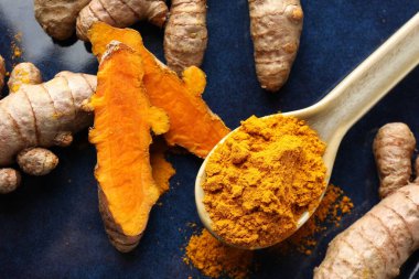 Kaşıkta aromatik zerdeçal tozu ve mavi tabakta taze kökler.