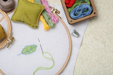 Embroidery and different sewing accessories on beige textured table, flat lay