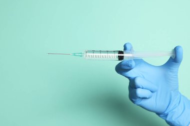 Doktorun elinde turkuaz arka planda ilaç içeren şırınga var. Yakın plan. Metin için boşluk