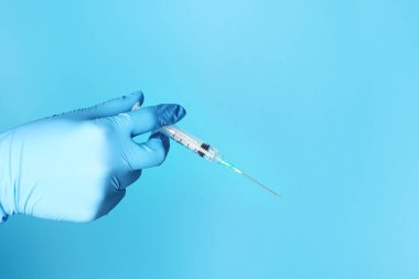 Doktor açık mavi arka planda şırınga tutuyor, yakın plan. Metin için boşluk