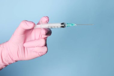 Tozlu açık mavi arka planda ilaçlı şırınga tutan doktor, yakın plan.