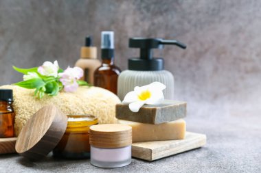 Gri masada farklı vücut bakım ürünleri ve çiçekler, yakın plan.