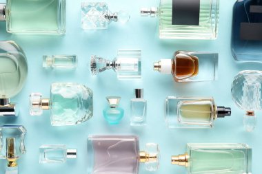 Bottles of various perfumes on light blue background, flat lay