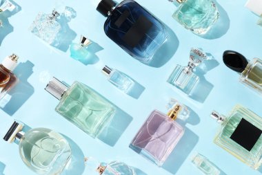 Bottles of various perfumes on light blue background, flat lay