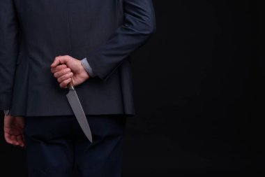 Siyah arka planda sırtında bıçak tutan bir iş adamı, yakın plan. Metin için boşluk