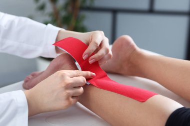 Hastanedeki hastanın ayağına Kinesio bantları takan doktor.