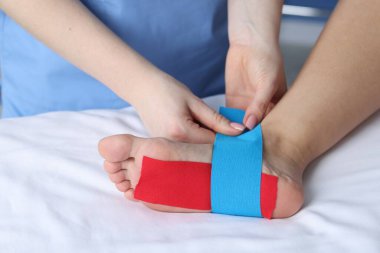 Hastanedeki hastanın ayağına Kinesio bantları takan doktor.