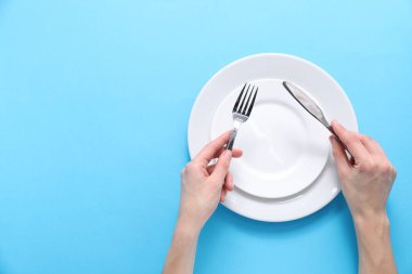 Açık mavi arka planda boş tabaklar üzerinde çatal bıçak takımı olan bir kadın. Metin için boşluk