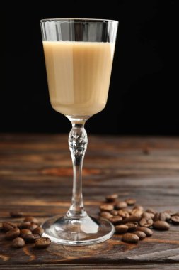 Bardakta kremalı kahve likörü ve ahşap masada fasulye, yakın plan.